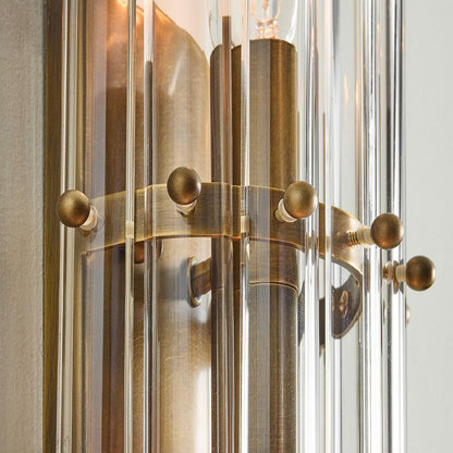 The Zeamas Wall Sconce's aged brass backplate complements the glass shade, reflecting the light with a subtle elegance, making this luminaire a statement piece that enhances the aesthetic of any interior.